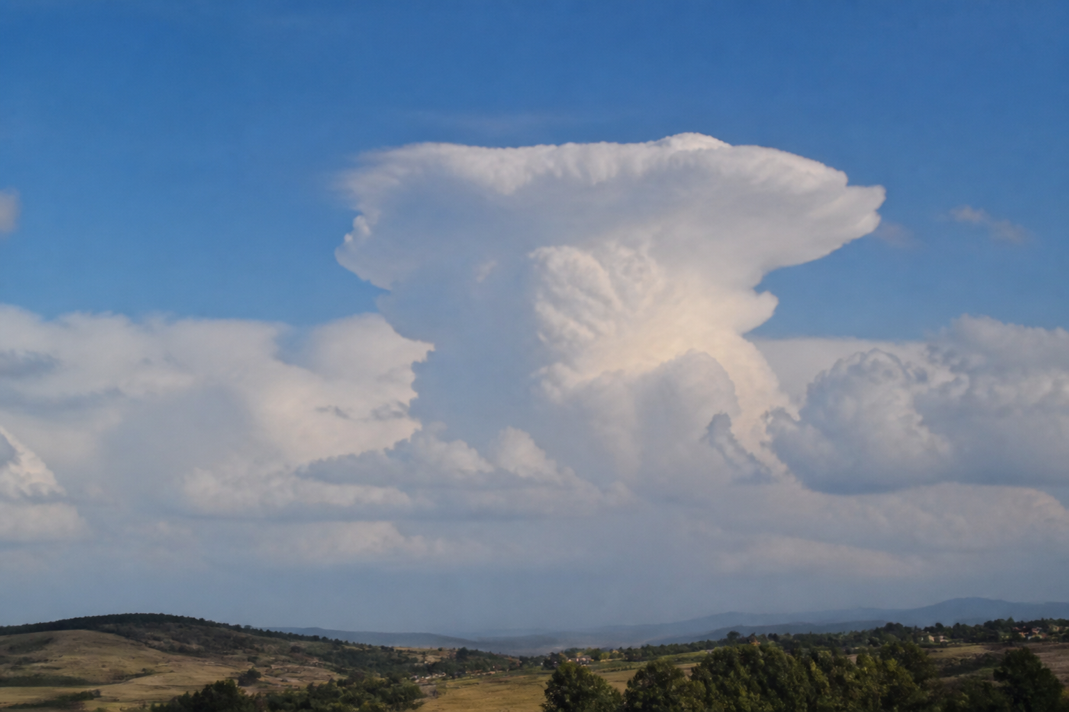 Cumulonimbus vu de loin, tour blanche dont le sommet s'étale en enclume fibreuse au-dessus d'une base sombre et pluvieuse